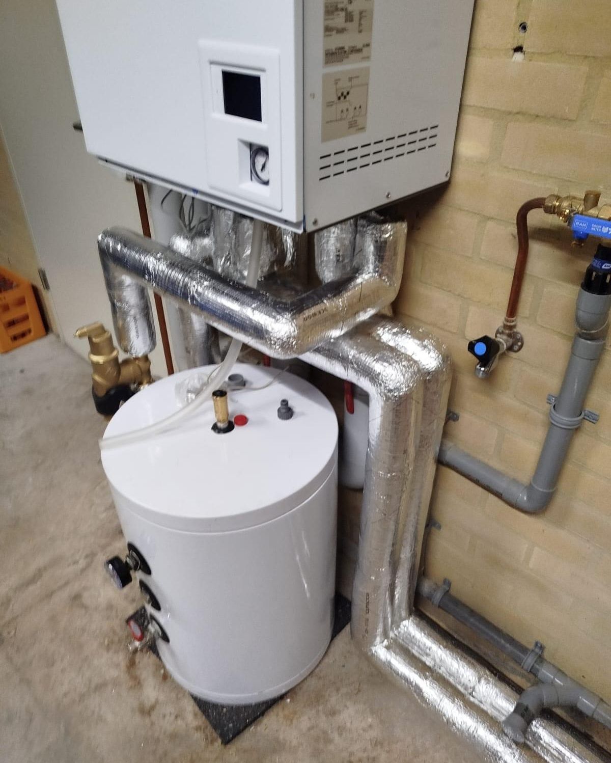 Insulated pipework around a heat pump and buffer tank in a residential plant room